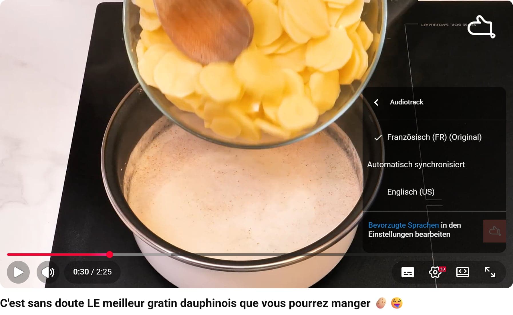 Das Audiotrack-Menü im YouTube-Player mit deutscher Oberfläche: Französisch (FR) (Original) ist ausgewählt, darunter die Gruppe Automatisch synchronisiert mit Englisch (US) und der Link Bevorzugte Sprachen in den Einstellungen bearbeiten