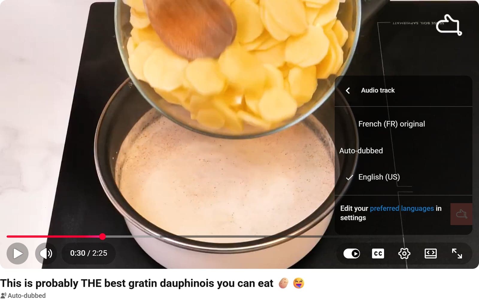 YouTube player with the Audio track menu open: French (FR) original, and English (US) checked under Auto-dubbed. Below the video, an English title and an Auto-dubbed label